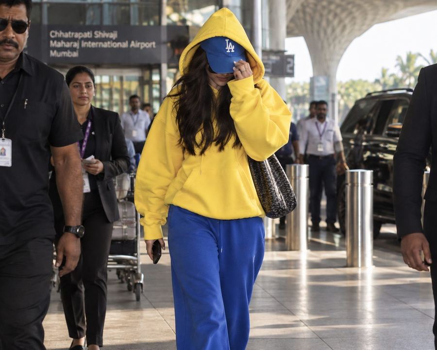 Celebrity arriving at Mumbai airport in a yellow hoodie, surrounded by a security team